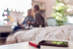 a vape and a phone on a side table with two teens in the background to show signs your teen is vaping