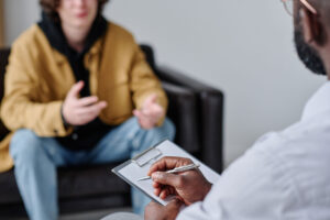 a teen talks to a therapist while sitting in a chair about teen partial hospitalization program