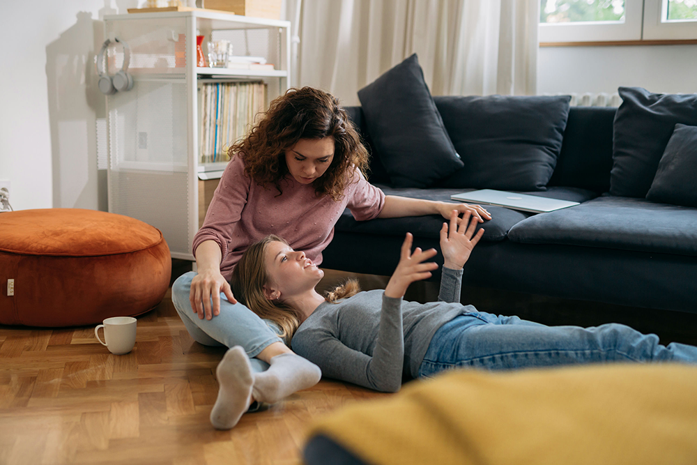 Parent gently talking to a teen on the floor, showing support and open communication about mental health
